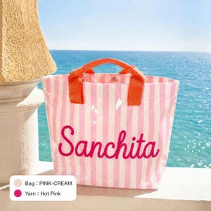 May include: A tote bag featuring vertical pink and cream stripes with two orange handles. The name Sanchita is embroidered in hot pink script across the front. A small color legend box in the corner indicates the bag is pink-cream and yarn is hot pink.