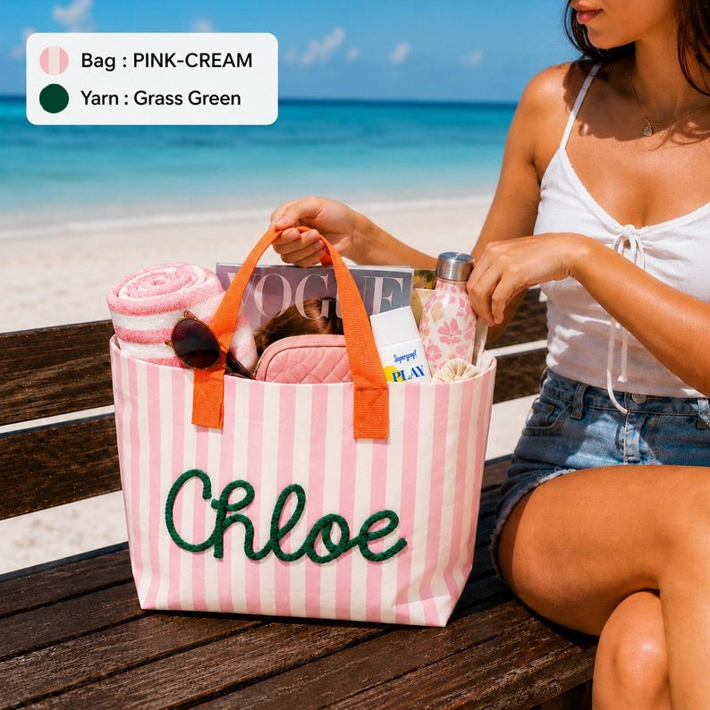 K&ouml;nnte beinhalten: Eine rosa-cremefarbene gestreifte Tragetasche mit orangefarbenen Henkeln und dem Namen Chloe in grasgr&uuml;nem Garn auf der Vorderseite. Die Tasche enth&auml;lt ein rosa-wei&szlig; gestreiftes Handtuch, ein Magazin, ein kleines rosa Etui, eine Sonnencreme und eine Trinkflasche.