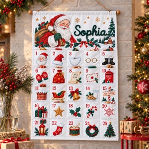 May include: A white fabric Christmas advent calendar featuring a hanging design with the name Sophia printed in green. It displays a Santa Claus illustration and twenty-five numbered pockets, each decorated with festive icons like gifts, a sleigh, and a tree.