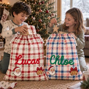 Pode incluir: Dois sacos de presente de Natal em tecido com padrão xadrez. Um saco tem xadrez vermelho com o nome Lucas em letras vermelhas e um rosto de Pai Natal com sinos. O outro tem xadrez azul com o nome Chloe em letras verdes e sinos.