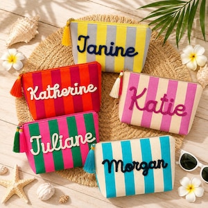 Può includere: Cinque pochette rettangolari con cerniera a righe verticali gialle e grigie, rosse e arancioni, rosa e crema, verdi e rosa, e blu e crema. Ogni pochette presenta un nome personalizzato ricamato in corsivo e una nappa coordinata.
