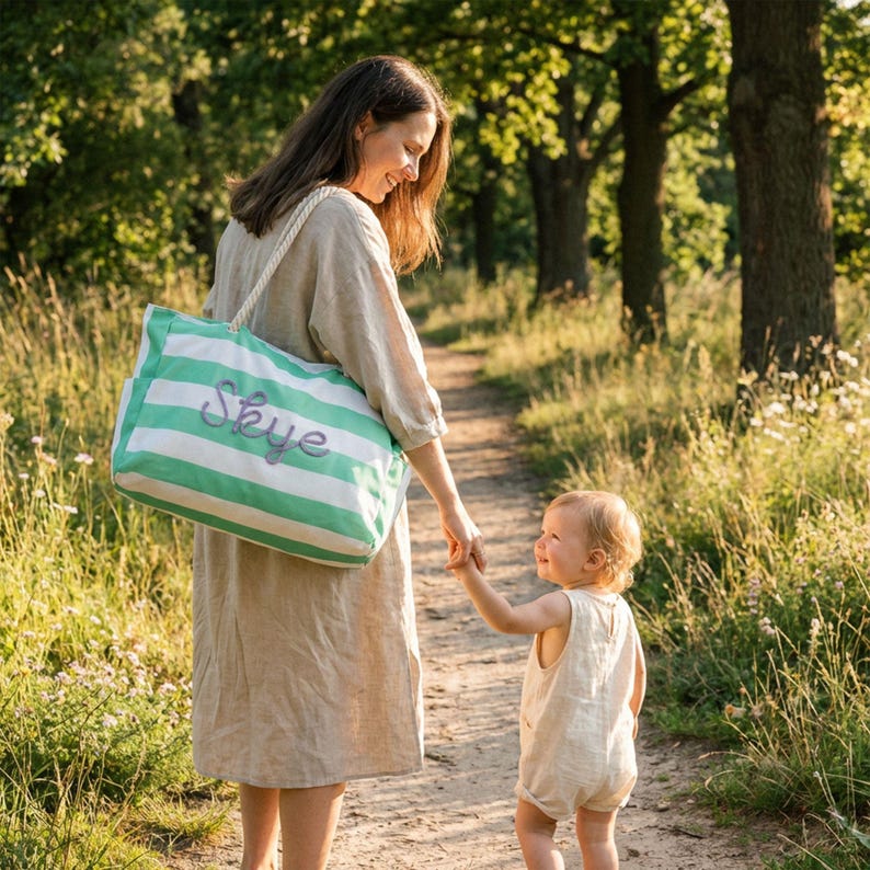 Mother and child walking in a park, mom is wearing a custom green striped canvas tote bag with zipper, a great personalized Mother's Day gift for mom
