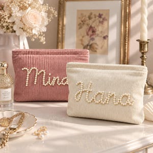 May include: Two rectangular corduroy pouches, one dusty pink and one cream, each featuring a name written in white faux pearls. The pink pouch displays the name Mina, while the cream pouch displays the name Hana in cursive script lettering.