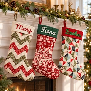 Peut inclure: Trois chaussettes de Noël personnalisées suspendues. La première a un revers crème avec le nom Mary et un motif chevron rouge et vert. La deuxième a un revers vert avec le nom Fiona et une scène hivernale rouge. La troisième a un revers rouge avec le nom Booker et un motif de triangles multicolores.