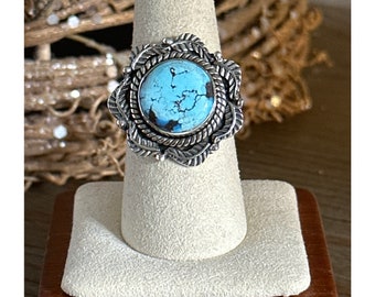 May include: A silver ring with a turquoise stone set in a detailed, ornate design. The ring is displayed on a white ring stand.