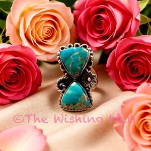 May include: A silver ring with two turquoise triangle-shaped stones. The ring is surrounded by pink and peach roses. The text "The Wishing Well" is visible in the image.