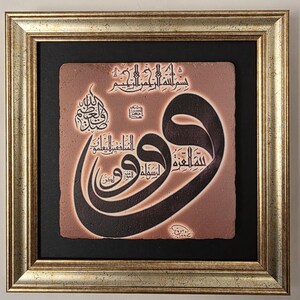 Op de afbeelding: Een ingelijst kunstwerk met zwarte Arabische kalligrafie op een roodbruine achtergrond. De kalligrafie is sierlijk en gedetailleerd, met een goudkleurige lijst en een zwarte passe-partout. Het kunstwerk is vierkant.