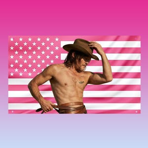 Può includere: Una bandiera americana rosa e bianca sullo sfondo. Una persona indossa un cappello da cowboy marrone e tiene una cintura di cuoio. La persona è a torso nudo. La bandiera presenta stelle e strisce bianche.