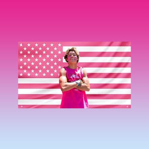 May include: A pink American flag with white stars and stripes is displayed behind a person wearing a pink tank top. The person has their arms crossed and is smiling. The tank top has text on it.