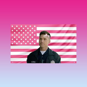 以下が含まれることがあります： ピンク色の星条旗を背景に、警察の制服を着た男性が立っています。彼の頭にはピンクのリボンが付いています。旗には白い星と縞模様があります。男性の制服には「Bradford」という名前が書かれています。