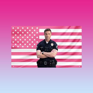 Puede incluir: Una bandera estadounidense rosa con estrellas y rayas blancas en el fondo. Una persona con uniforme de policía azul oscuro está de pie frente a la bandera con los brazos cruzados. El uniforme tiene una placa y un reloj.