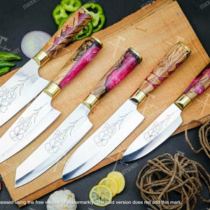 Puede incluir: Un juego de cinco cuchillos de cocina de acero inoxidable con hojas grabadas con motivos florales y mangos de madera coloridos. Los mangos tienen virolas doradas. Los cuchillos están colocados sobre una tabla de cortar de madera, con verduras y cuerda cerca.