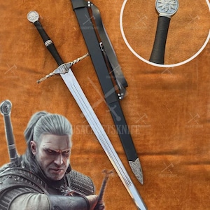 May include: A silver and black sword with a long, double-edged blade and a black handle. The sword is accompanied by a black sheath with silver accents. The hilt features a circular emblem. The image also includes a close-up of the sword's handle and a character from the Witcher series.