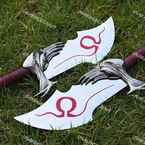 May include: Two silver-colored blades with a red handle and a stylized hand-shaped guard. The blades have a curved design with a red Omega symbol. The blades are displayed on a bed of green grass.
