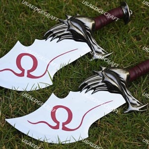 May include: Two decorative fantasy swords with silver-colored blades and handles wrapped in burgundy leather. The blades have a white surface with a red omega symbol. The swords are lying on a bed of green grass.
