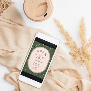 May include: A smartphone displays a "Mahjong Party" invitation against a green floral background. The invitation features a pink oval with text and Mahjong tile graphics. A beige coffee cup and fabric are also in the image.