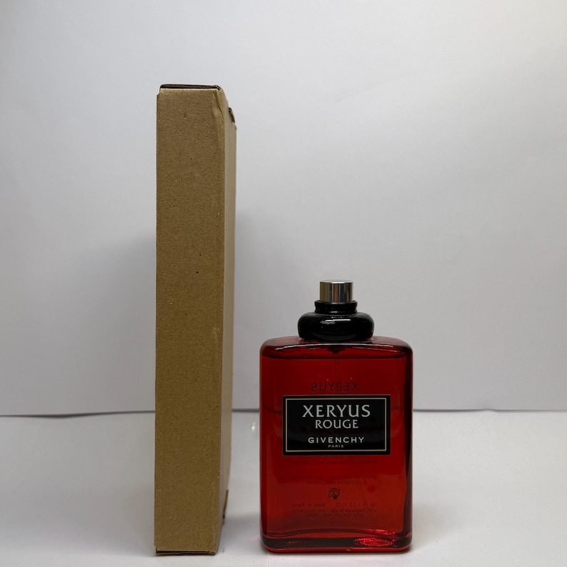 Puede incluir: Un frasco de perfume rectangular rojo con tapa negra y detalles plateados. El frasco tiene una etiqueta que dice "XERYUS ROUGE GIVENCHY PARIS". A la izquierda del frasco hay una caja de cart&oacute;n alta y estrecha.