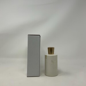May include: A white perfume bottle with a gold cap and a matching white box. The bottle has a cylindrical shape and the text "Juliette" is printed on the front. The box is rectangular and has a dark brown top.