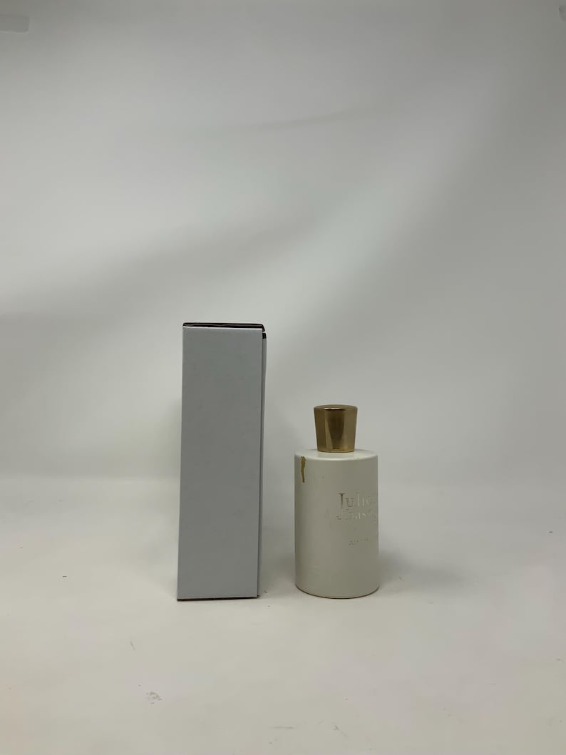 May include: A white perfume bottle with a gold cap and a matching white box. The bottle has a cylindrical shape and the text "Juliette" is printed on the front. The box is rectangular and has a dark brown top.