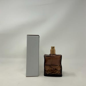 Puede incluir: Un frasco de perfume de vidrio marrón con un pulverizador dorado y la palabra "BOSS" impresa en la parte delantera. Una caja rectangular blanca está al lado del frasco. El frasco de perfume tiene un diseño texturizado.