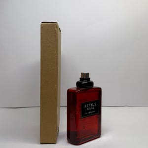Puede incluir: Un frasco de perfume rectangular rojo con tap&oacute;n negro y pulverizador plateado, junto a una caja de cart&oacute;n alta y estrecha. El frasco tiene una etiqueta que dice "XERYUS ROUGE GIVENCHY".