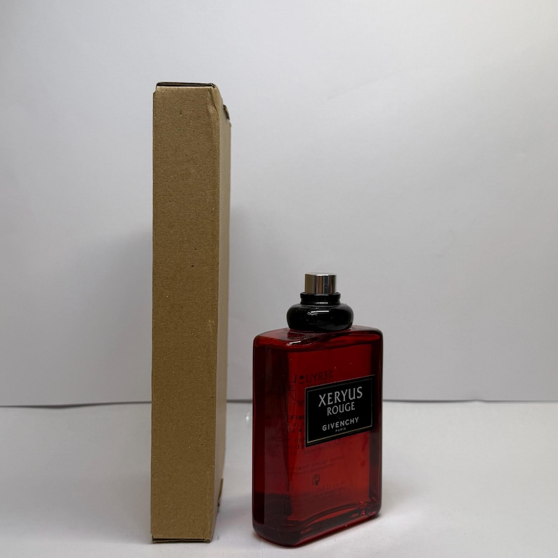 Puede incluir: Un frasco de perfume rectangular rojo con tap&oacute;n negro y pulverizador plateado, junto a una caja de cart&oacute;n alta y estrecha. El frasco tiene una etiqueta que dice "XERYUS ROUGE GIVENCHY".
