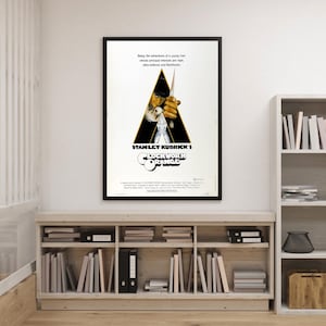 Pode incluir: Cartaz emoldurado do filme "Laranja Mecânica" de Stanley Kubrick. O cartaz apresenta um design triangular com uma figura segurando uma arma sobre um fundo preto. O título do filme é exibido de forma proeminente.