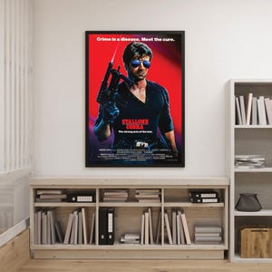 May include: A framed movie poster for "Cobra" starring Sylvester Stallone. The poster has a red backdrop with Stallone holding a firearm. The text "Crime is a disease. Meet the cure." is at the top. The title "Cobra" is displayed.