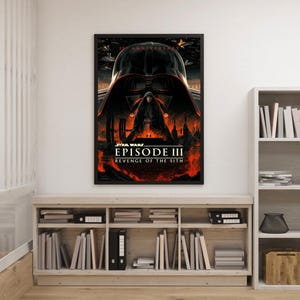 Op de afbeelding: Een ingelijste filmposter voor Star Wars: Episode III - Revenge of the Sith. De poster toont Darth Vaders helm in zwart- en roodtinten, met de titel van de film en een vurige achtergrond. De poster wordt op een lichtgekleurde muur getoond.