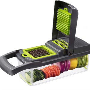 May include: A gray and green vegetable chopper with a clear container holding sliced vegetables. The chopper has multiple blades for dicing and slicing. The container holds sliced cucumber, carrot, red onion, lemon, and zucchini.