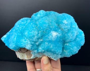 Puede incluir: Un vibrante espécimen mineral cristalino con un llamativo color turquesa brillante. El mineral tiene una apariencia texturizada y burbujeante, con una superficie rugosa e irregular. La base del espécimen es de un color marrón y blanco contrastante.