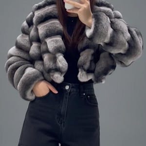 A person is taking a selfie with a grey and black fur coat, black shorts, and a black top.
