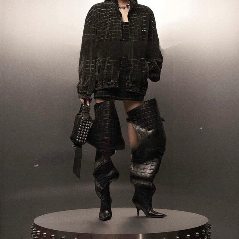 black, over-the-knee boots. Left boot has a crocodile texture with a buckle detail near the knee, and a stiletto heel. Right Boot is smooth black leather, slouching down, with a stiletto heel