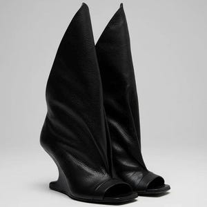 Puede incluir: Un par de botas negras de cuero con tacón de cuña. Presentan un diseño de punta abierta y cañas altas y drapeadas. Los tacones de cuña ofrecen un aspecto moderno y arquitectónico. Una elección audaz para los amantes de la moda.