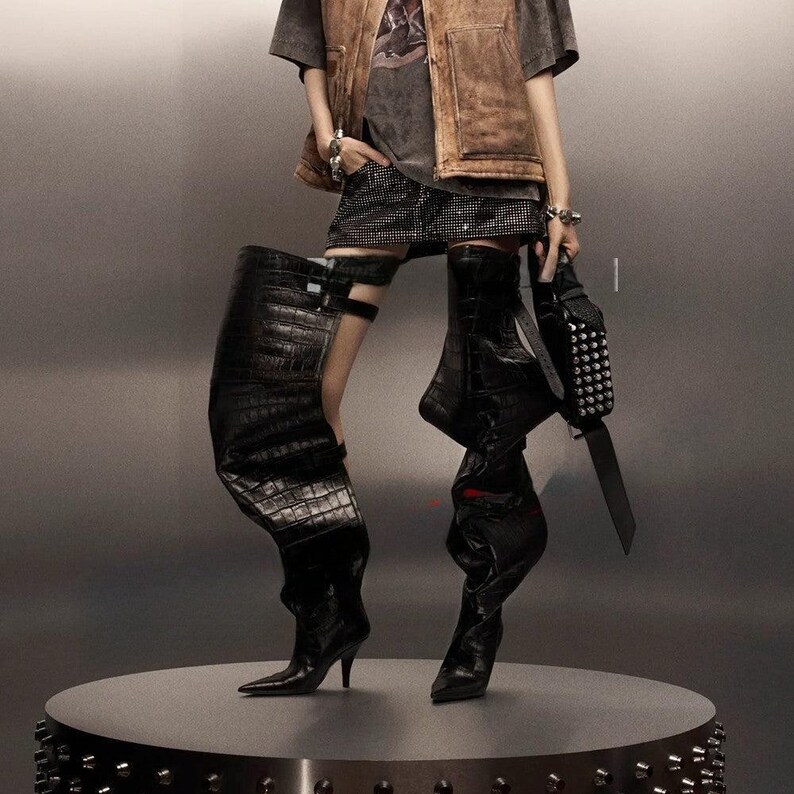 black, over-the-knee boots. Left boot has a crocodile texture with a buckle detail near the knee, and a stiletto heel. Right Boot is smooth black leather, slouching down, with a stiletto heel