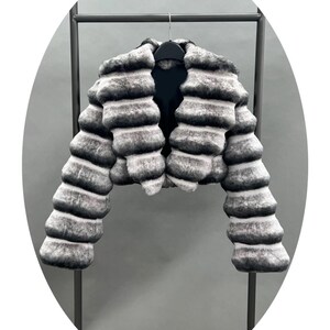A black and white fur coat is hanging on a black metal hanger against a gray background.