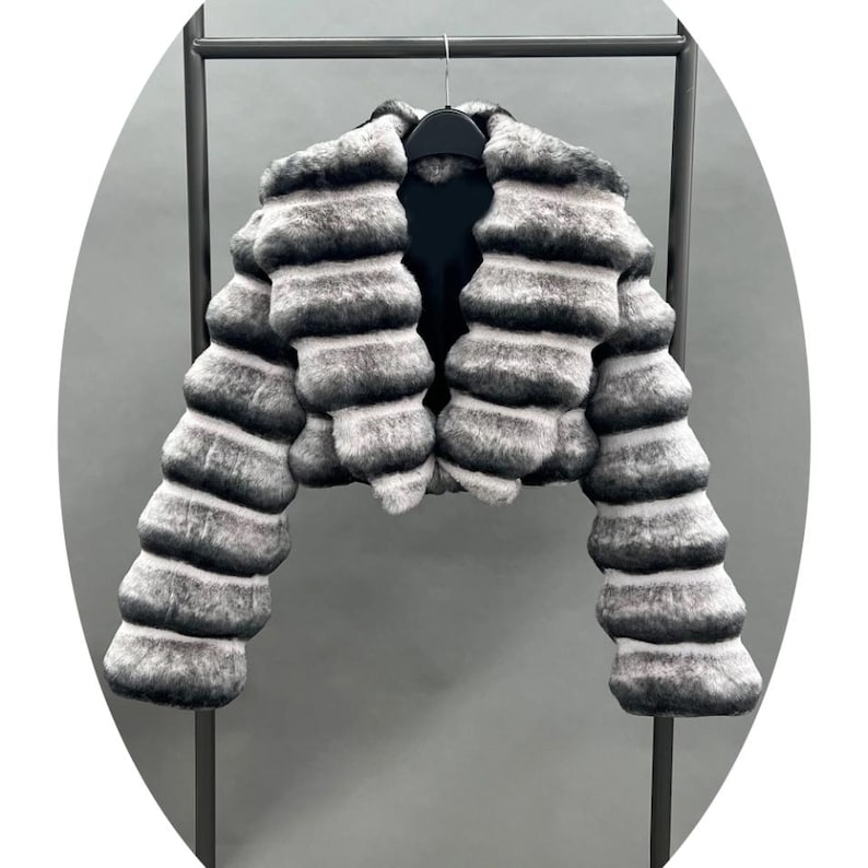 A black and white fur coat is hanging on a black metal hanger against a gray background.
