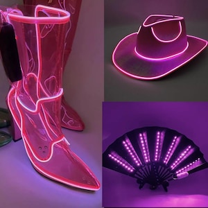 Può includere: Un set di accessori composto da un paio di stivali rosa trasparenti con profili luminosi al neon rosa, un cappello da cowboy rosa delineato da luce al neon rosa e un ventaglio pieghevole nero illuminato da luci LED rosa su ogni stecca.