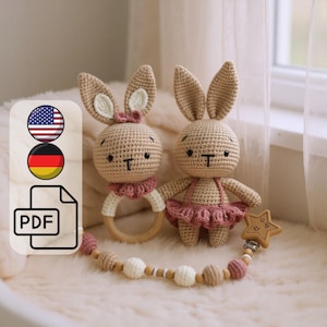 May include: Two crocheted bunny toys with tan bodies, pink accents, and wooden accessories. One bunny holds a wooden ring, the other a star-shaped teether. The bunnies have long ears and are on a soft, light-coloured surface.