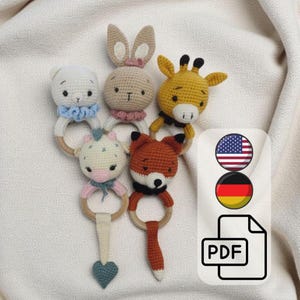 May include: A collection of five handmade crochet baby rattles in the shape of animals: a bear, bunny, giraffe, horse, and fox. Each rattle features a wooden ring and is crafted in soft, pastel colors.