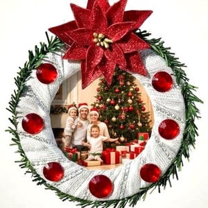 May include: A Christmas ornament shaped like a wreath, featuring a family photo. The wreath is decorated with red gems, green faux pine, and a glittery red poinsettia. A jute string is attached for hanging.