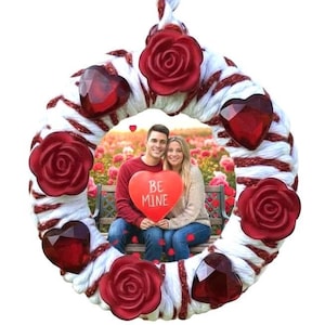 May include: A Valentine's Day wreath with a photo of a couple holding a heart-shaped sign that says "BE MINE." The wreath is decorated with red roses and heart-shaped gems, and white and red rope.