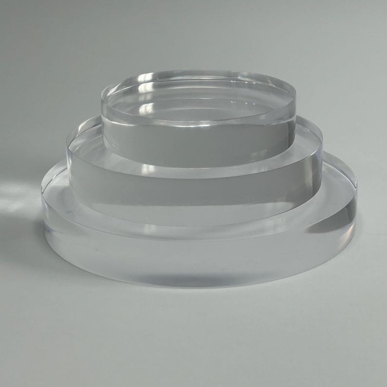 May include: A clear acrylic display stand featuring three circular levels. The stand is designed for product presentation, with each tier reducing in size upwards. The transparent material provides a clean, contemporary look.