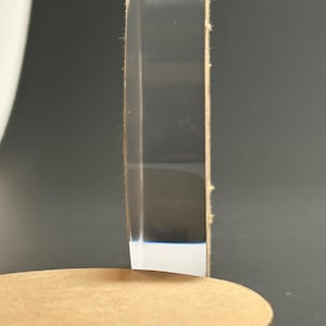 May include: A clear acrylic display stand with a round base. The stand is made of clear acrylic and has a light brown edge. The base is a light brown color. The stand is designed to hold an object.