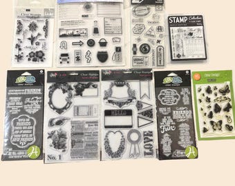 May include: A collection of clear stamps in various designs, including floral, travel-themed, and decorative elements. The stamps are packaged in clear plastic and feature words like "Hello," "Love," and "Friends."