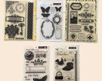 May include: Five clear stamp sets with various designs. The sets include stamps with butterflies, frames, clocks, and text like "Remember," "Family," and "Soar." The stamps are packaged in clear plastic with decorative backing cards.