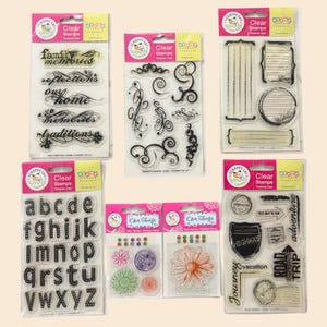 May include: A collection of clear stamps in various designs. The stamps include cursive words like "family memories" and "traditions", decorative swirls, an alphabet, floral designs, and travel-themed images with text like "vacation" and "road trip".