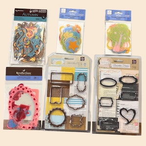 May include: A collection of craft supplies, including die-cut shapes and decorative frames. The packages feature various colors and designs, with some labeled "Autumn" and "Decorative Frames". The frames come in different shapes, including rectangles, ovals, and hearts.