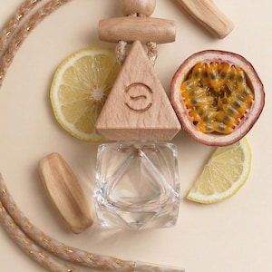May include: An aromatherapy diffuser with a wooden triangle and a clear glass container. The image includes a passion fruit half, lemon slices, and wooden sticks. A beige rope with gold accents is also present.