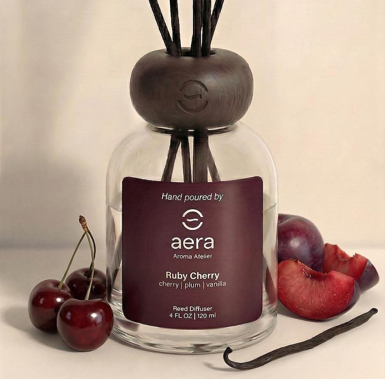 Peut inclure: Diffuseur de roseaux en verre avec un bouchon en bois fonc&eacute; et des roseaux. L'&eacute;tiquette indique "Ruby Cherry" avec des senteurs de cerise, prune et vanille. Des cerises fra&icirc;ches, des tranches de prune et une gousse de vanille sont dispos&eacute;es autour du diffuseur. Contenance 120 ml.